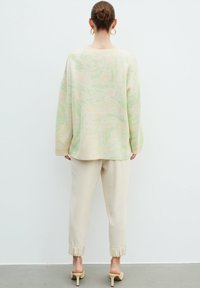 Maglione crema oversize con vortici verdi; pantaloni beige larghi con orli arricciati; indossati con sandali beige con tacco. Design semplice e accogliente.