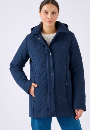 Giacca trapuntata blu navy con cappuccio, caratterizzata da un motivo a zigzag, bottoni a pressione e tasche laterali. Realizzata in un tessuto morbido e testurizzato.