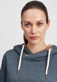 Felpa con cappuccio in tessuto blu scuro con un interno accogliente, caratterizzata da accenti beige, lacci crema e un design a collo incrociato.