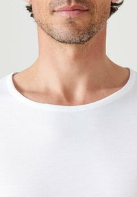 T-shirt bianca con una trama morbida, collo rotondo e design aderente, caratterizzata da una superficie liscia e uniforme senza motivi o dettagli visibili.