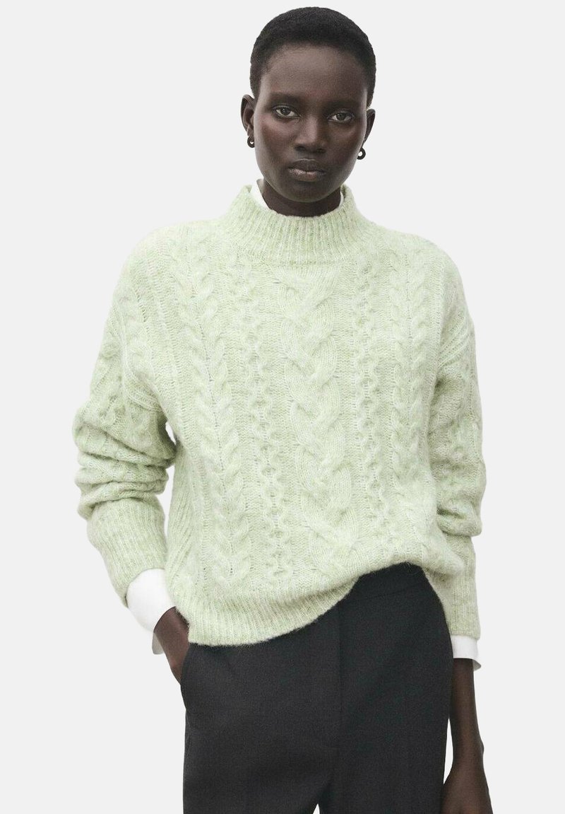 Svijetlozeleni džemper od pletenja s visokim okovratnikom i ležernim krojem. Rebrasti manžeti i rub. Uparen s tamnim hlačama i bijelom košuljom ispod.