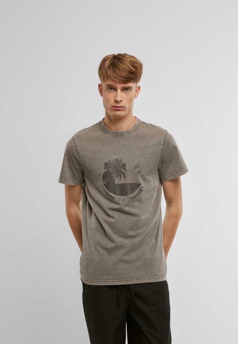T-shirt gris à manches courtes en coton doux avec un graphique de palmier et des détails textuels. Coupe décontractée et texture légèrement usée.
