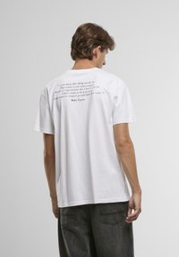 Balta kokvilnas T-kreklā aizmugurē ir melns citāts. Īsas piedurknes, apaļš kakls un brīva piegriezuma.