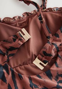 Braunfarbener Stoff mit schwarzem abstraktem Muster, mit fransigen Kanten, verstellbaren Trägern und goldenen Metallverschlüssen. Glatte Textur und taillierte Passform.