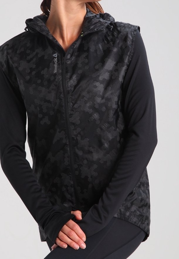 Czarna kurtka z kapturem o teksturowanym wzorze w kamuflaż. Posiada pełny zamek i długie rękawy z otworami na kciuki dla pewnego dopasowania. Widoczne logo Reebok.
