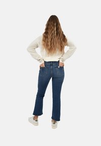 Jeans a palazzo blu a vita alta con un design discreto della tasca posteriore, abbinati a un maglione di colore chiaro e sneakers metalliche.