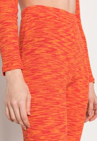 Leggings texturizados em vermelho e laranja com um padrão de rede, apresentando uma cintura alta e um design ajustado. Tecido suave com material elástico.