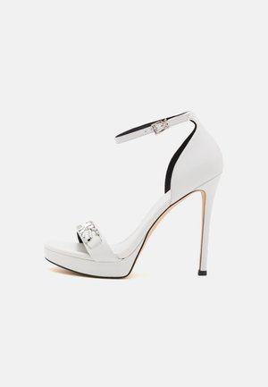 Hvid højhælet sandal med ankelrem, plateau-sål, åben tå og sølvfarvet dekorativ spænde på tå-remmen.