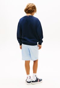 Μπλε σκούρο φούτερ με στρογγυλή λαιμόκοψη, συνδυασμένο με ανοιχτό μπλε σορτς. Διαθέτει αντίθετη κόκκινη ρίγα στο πίσω μέρος της λαιμόκοψης.