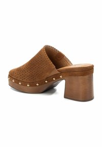Zoccolo in suede marrone con design perforato, dotato di un tacco in legno spesso, borchie dorate lungo la base e dettagli cuciti sulla parte superiore.
