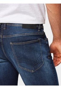 Tummansininen farkut, joissa on suora leikkaus, kontrastitikkaukset ja merkitty musta nahkapatentti vyötäröllä.