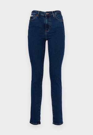 Jeans in denim blu scuro con vestibilità skinny, caratterizzati da vita media, passanti per cintura, cinque tasche e una leggera texture sbiadita.
