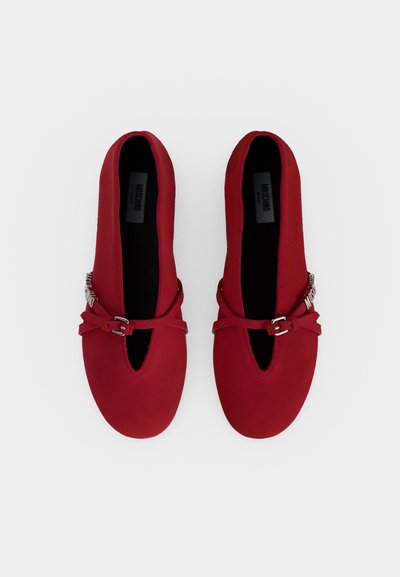Paire de chaussures plates rouges avec bouts pointus et fines brides à boucles, vues de dessus sur un fond clair uni.