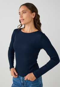 Navy lange mouwen top in ribstof met een ronde hals. Aansluitende pasvorm met textuur details en smalle mouwen. Gecombineerd met blauwe denim.