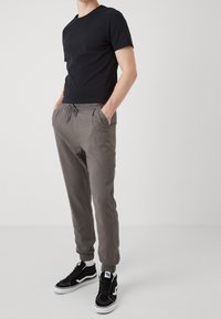 Svart t-shirt med kort ärm som matchas med grå joggers med elastisk midja och svarta högskurna sneakers med vita detaljer och texturerade ytor.