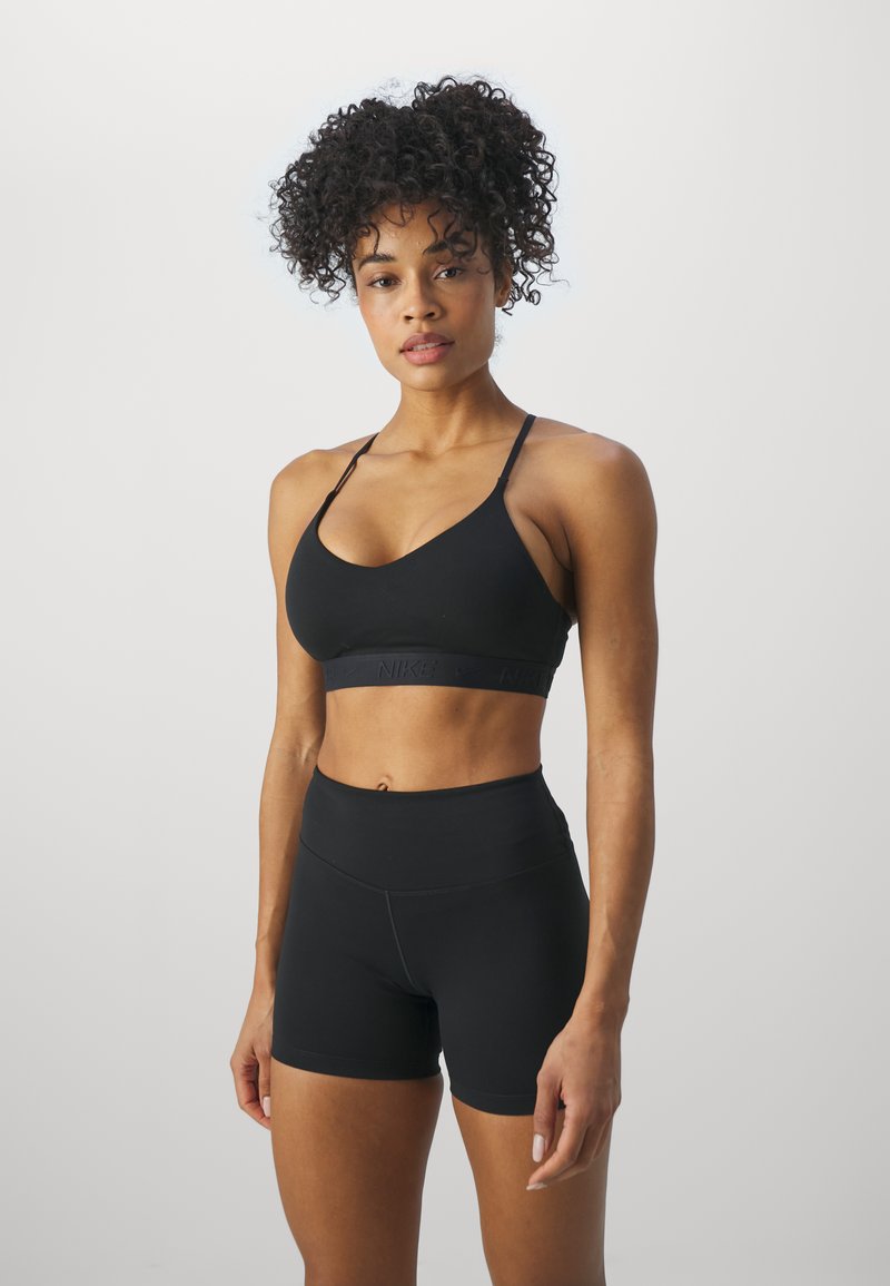 Zwarte sportbeha met een brede tailleband met reliëflogo, gecombineerd met hoge zwarte shorts. Beide zijn aansluitend en hebben een gladde textuur.