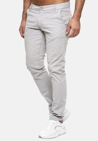 Jasnoszare chinosy o wąskim kroju z ozdobnym przeszyciem, przednimi kieszeniami i zapięciem na guzik, zestawione z białymi butami sportowymi.