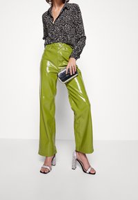 Black blouse with white polka dots, green glossy wide-leg pants, and silver clutch. Sparkly block-heel sandals complete the look.