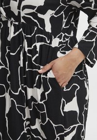Vestido en blanco y negro con un patrón abstracto, mangas largas, cintura fruncida y bolsillos laterales, hecho de un material suave y elástico.