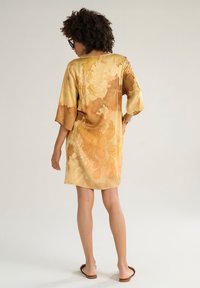 Kaftano in satin con una vestibilità ampia, caratterizzato da un motivo tie-dye nei toni dell'arancione e del giallo. Maniche corte e scollatura rotonda.