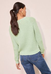 Hellgrüner Strickpullover mit strukturiertem Design, gerippten Ärmelbündchen und Saum, kombiniert mit dunkelblauen Jeans. Verfügt über eine lockere Passform.