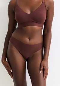Bruine stoffen bralette met dunne bandjes en bijpassende bruine bikini-stijl slips. Gladde textuur, naadloos design en gemiddelde bedekking.