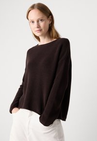 Maglione a coste marrone scuro con una vestibilità rilassata, scollatura a girocollo e maniche lunghe, abbinato a pantaloni chiari.
