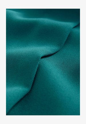 Teal Stoff mit glatter, matter Textur, der subtile Falten und Knicke zeigt, was auf ein leichtes und fließendes Material hinweist.