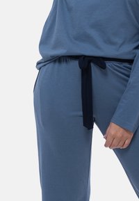 Sininen loungewear-setti, johon kuuluu pitkähihainen paita ja joustava vyötärönauhapari. Vyötärönauhassa on kontrastivärinen laivastonsininen solmuseikka. Pehmeä texture.
