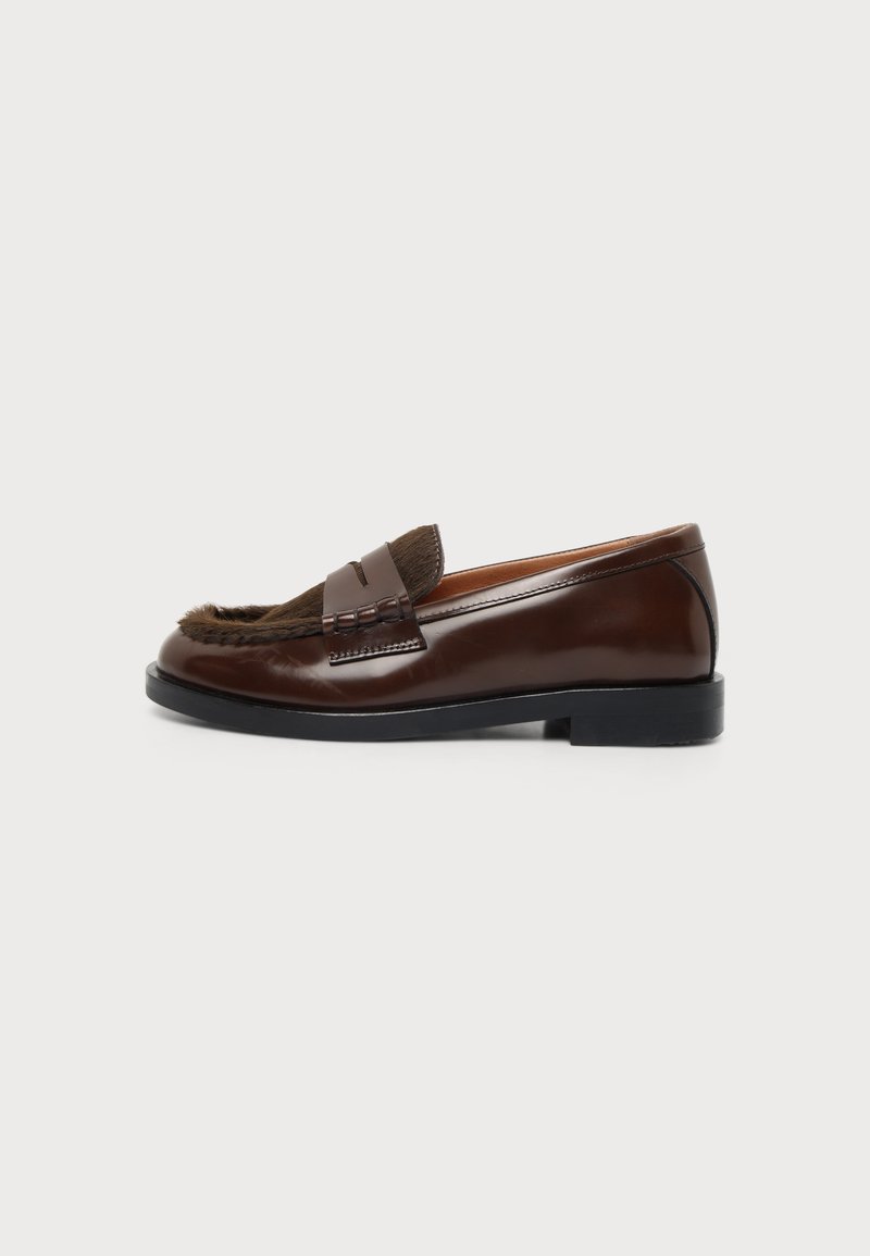 Mocassin en cuir marron avec semelle noire et détail en fourrure sur le dessus, vu de côté sur un fond clair uni.