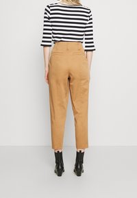 Tan hoge taille broek met een rechtlijnig ontwerp, voorzien van achterzakken en een soepele textuur, gecombineerd met een zwart-wit gestreepte top.
