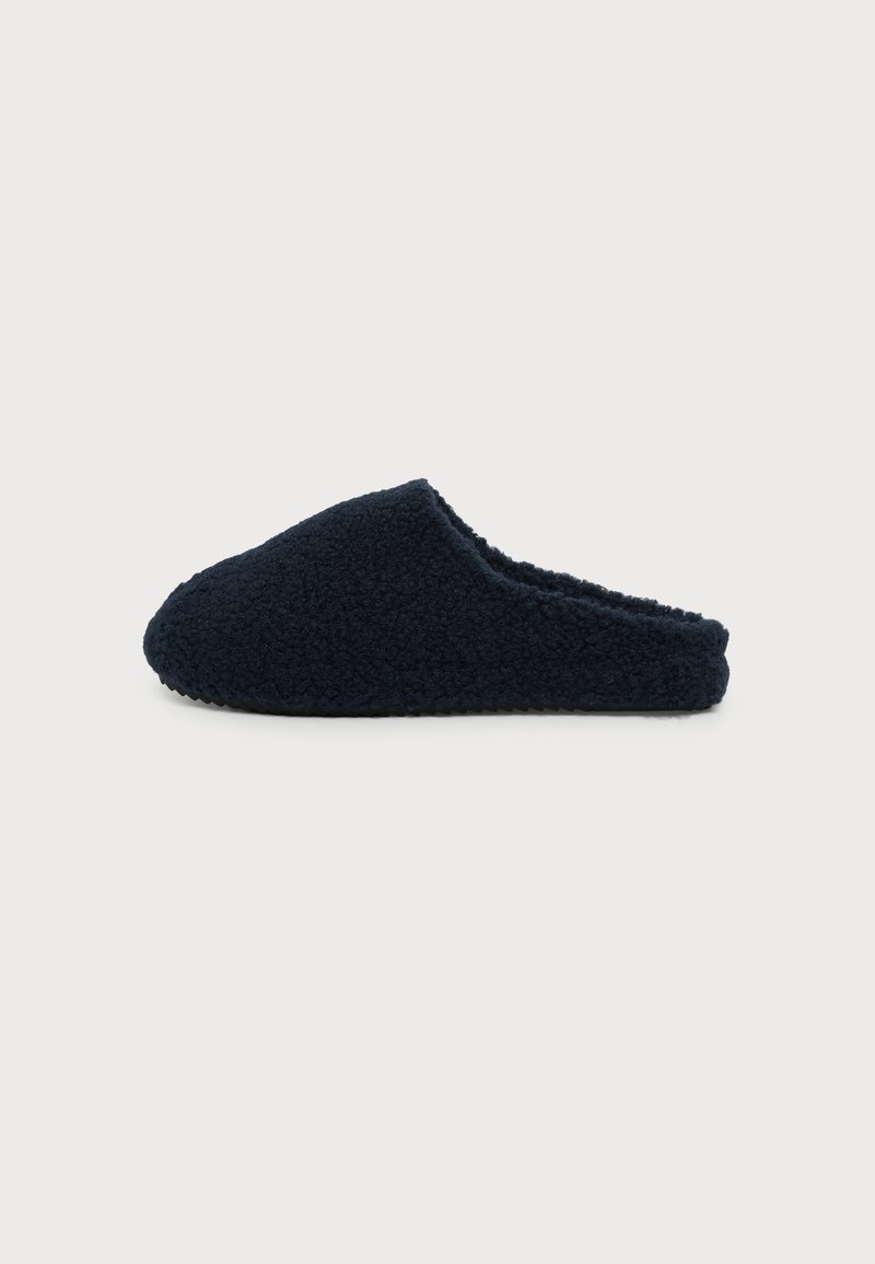 Μαύρο μοκασίνι τύπου slip-on με υφή, χνουδωτή εξωτερική επιφάνεια και κλειστή μύτη, εμφανίζεται προφίλ σε λευκό φόντο.