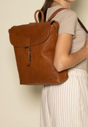 Brauner Leder-Rucksack mit umgeschlagenem Deckel, verstellbaren Trägern, Schnallenverschluss und einem geprägten Logo auf der Seite.