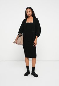 Μαύρο ριμπ μίντι φόρεμα συνδυασμένο με μια oversized μαύρη ζακέτα, καφέ τσάντα και μαύρες σандάλες με λουριά και αγκράφες.