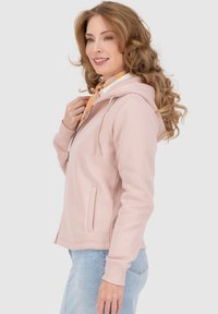 Felpa leggera rosa con zip, con coulisse, tasche laterali e polsini a coste. Indossata sopra una maglietta bianca con una sciarpa arancione.
