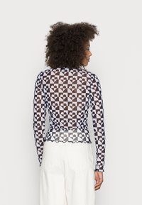 Top de mangas longas, transparente, com um padrão de corações em preto e branco, bainha em forma de onda e design ajustado. Combinado com calças brancas de cintura alta.