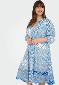 Modra in bela obleka s potiskom, z 3/4 rokavi, V-izrezom, gumbi spredaj in širšim krilom, ki vsebuje kompleksne cvetlične in geometrijske vzorce.