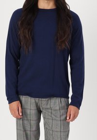 Chemise marine à manches longues en tissu doux avec un col rond. Associée à un pantalon à carreaux gris, présentant un motif classique à carreaux.