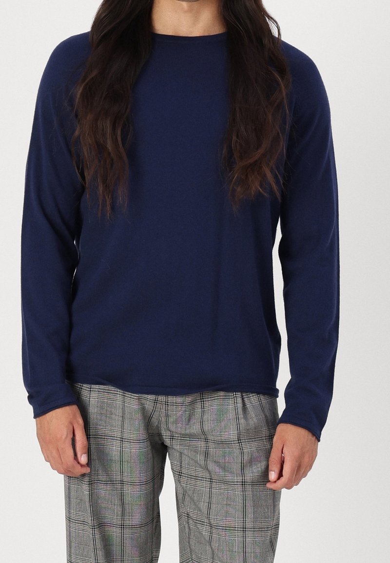 Chemise marine à manches longues en tissu doux avec un col rond. Associée à un pantalon à carreaux gris, présentant un motif classique à carreaux.