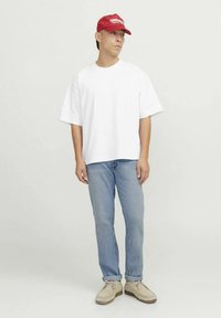 Valge lühikeste varrukatega t-särk, helesinised teksad ja beežid kingad. Punane nokamüts tikitud tekstiga. Lihtne disain, vaba lõige ja pehmed tekstuurid.