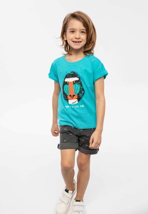 Camiseta turquesa de manga corta con un gráfico de la cara de un babuino en colores llamativos, combinada con pantalones cortos grises con estampado de animales.