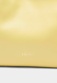 Sac à main en cuir synthétique jaune avec logo "LIU•JO" en relief, texture lisse et design minimaliste. Forme compacte adaptée à un usage décontracté.