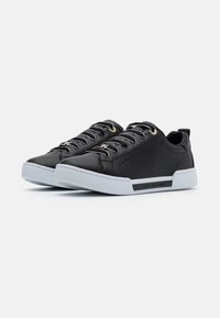 Ein Paar schwarze Low-Top-Sneaker mit weißen Sohlen, schwarzen Schnürsenkeln, metallischen Ösen und "Tommy Hilfiger"-Branding an der Seite.