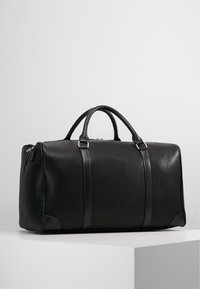 Black leather duffle bag with smooth texture, dual top handles, two accent straps, and a zip closure. Sturdy rectangular shape.