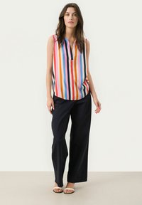 Sleeveless blouse with vertical multicolored stripes, paired with loose-fitting navy pants. Blouse features a V-neck and soft, smooth fabric.