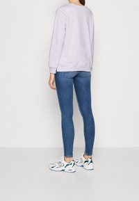 Felpa lilla chiaro con maniche lunghe, abbinata a jeans skinny blu e sneaker bianche con dettagli verdi e viola.