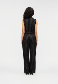 Combinaison noire sans manches avec des rayures blanches verticales, taille ceinturée, pantalons amples et tissu lisse et texturé.