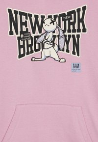 Sudadera rosa con un conejo de dibujos animados de ojos cruzados, texto "NEW YORK BROOKLYN" en negrita negra y una etiqueta "R.A.W SPORT" en la parte inferior.