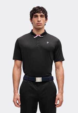 Mann trägt ein schwarzes kurzärmeliges Polo mit rosa und weißem Besatz am Kragen, schwarze Hose und einen marineblauen Gürtel mit silberner Schnalle.