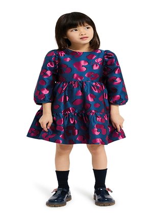Blauwe jurk met een roze abstract patroon, pofmouwen en een gelaagde rok. Gecombineerd met marineblauwe sokken en glanzende zwarte schoenen met accenten.